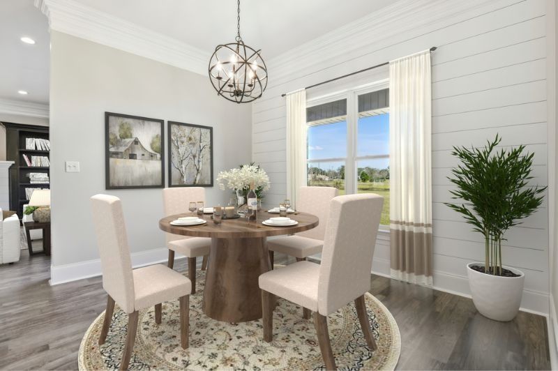 Dining room with round wooden table, chairs, art, and plant. White walls, gray floors.