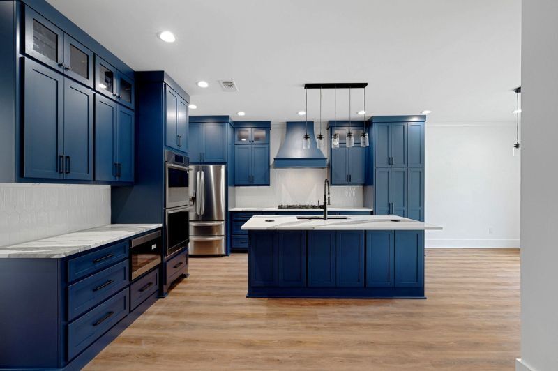 Blue kitchen with a central island, stainless steel appliances, and light wood floors.