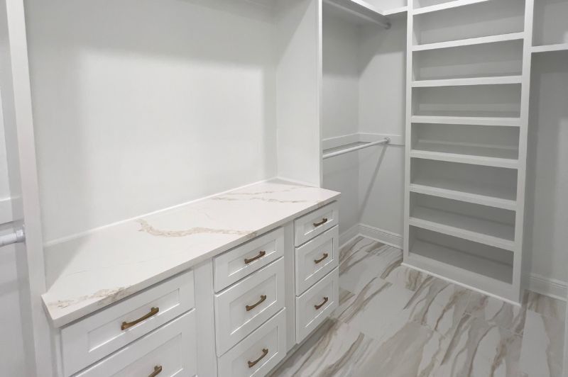 White walk-in closet with quartz countertop, built-in drawers, shelves, and a ladder for high shelves.