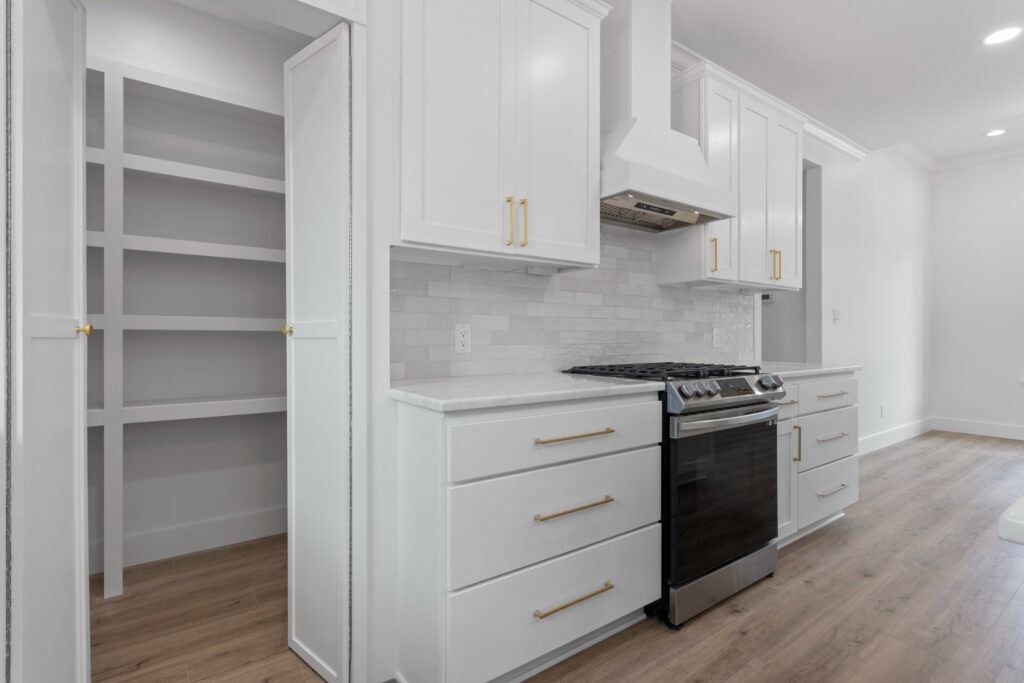 White kitchen with cabinets, pantry, and stainless steel appliances.