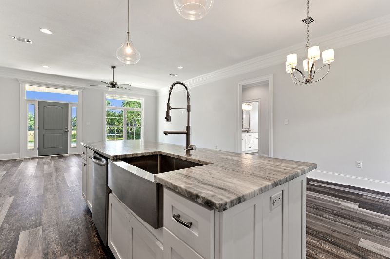 Modern kitchen with island, sink, and stainless steel appliances. Natural light, wooden floors, white cabinets.
