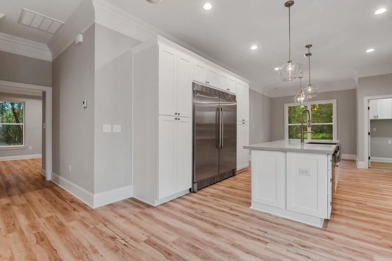 Modern kitchen with white cabinets, stainless steel fridge, gray walls, and wood floors.