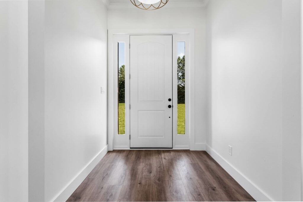 White entryway with wooden floor, door to outdoors with sidelights.