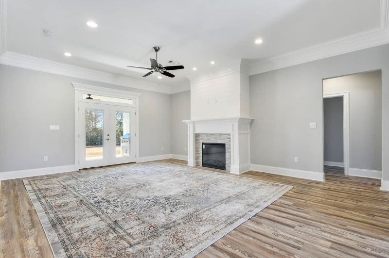 Spacious living room with fireplace, rug, hardwood floors, and French doors. Gray walls, white trim, and a ceiling fan.