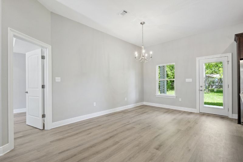 Empty, modern dining room with light gray walls, wood-look flooring, chandelier, and door to backyard.