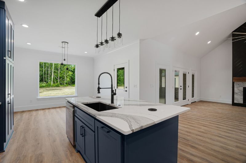 Modern kitchen with navy island, white countertops, and hardwood floors, overlooking a wooded view.