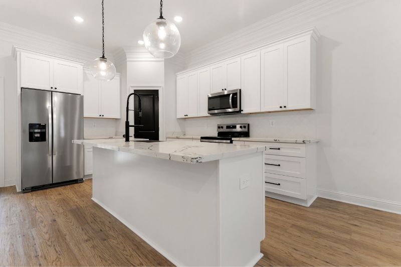 Modern white kitchen with island, stainless steel appliances, and light wood floors.