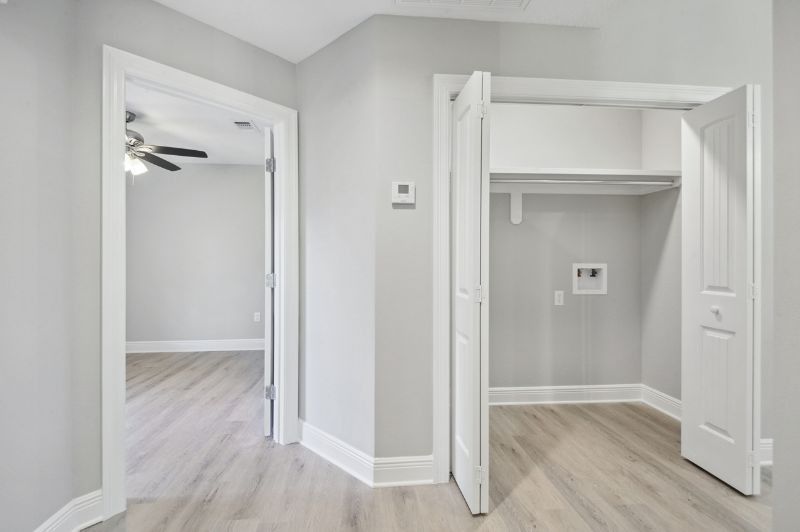 Hallway with open closet and doorway to a bedroom with light gray walls, light wood floors.