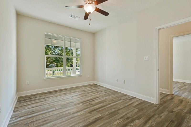 Empty room with wooden floor, window, door, and ceiling fan.