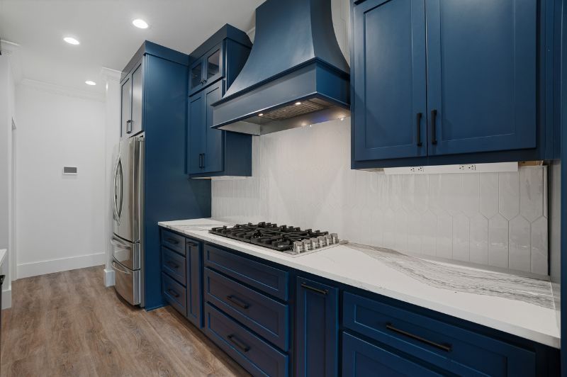 Blue kitchen with white countertops and backsplash, stainless steel appliances, and light wood flooring.