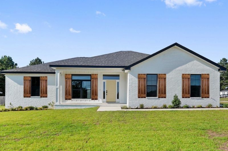 White brick house with brown shutters, front lawn, and blue sky.