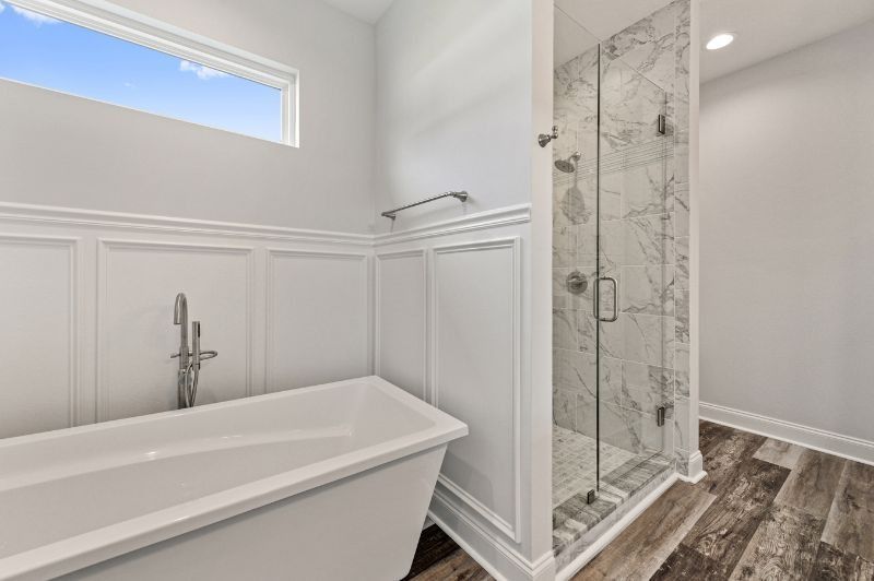 Modern bathroom with a white tub, glass shower, and marble tile, with wood-look flooring.