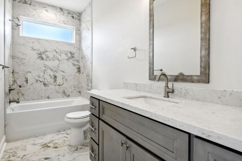 Bathroom with marble-look tile, gray vanity, white countertop, large mirror, and bathtub.