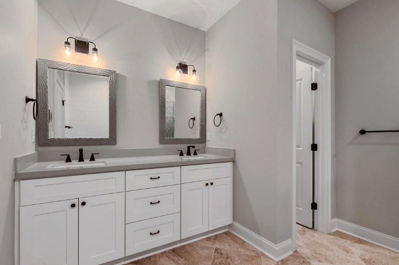 Bathroom with white cabinets, gray countertops, two mirrors, and a doorway.
