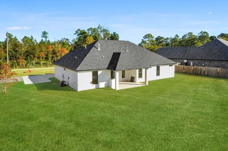 Back of a single-story, white brick house with a dark roof, on a large green lawn under a blue sky.