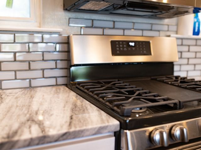 Stainless steel gas range on a marble countertop with a grey subway tile backsplash in a kitchen.