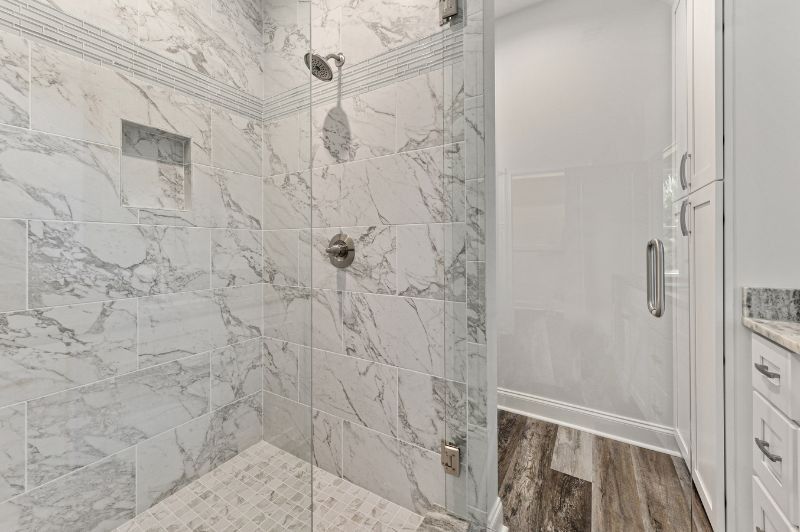 Marble-tiled shower with glass door; interior white cabinets and wood-look flooring in a bathroom.