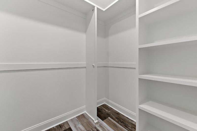 Empty white closet with shelves and a section with a rod. Wood-look flooring.