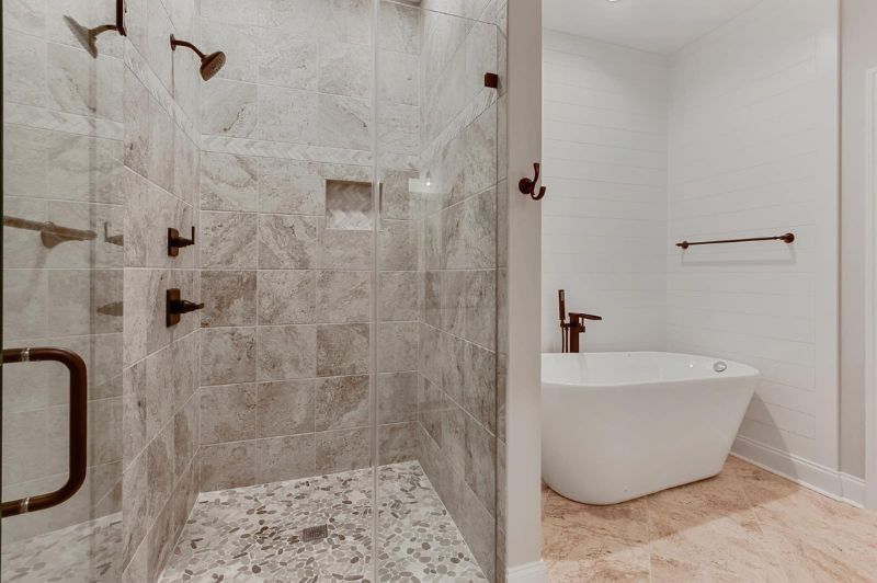 Bathroom with a glass shower and standalone tub. Beige tile and bronze fixtures.