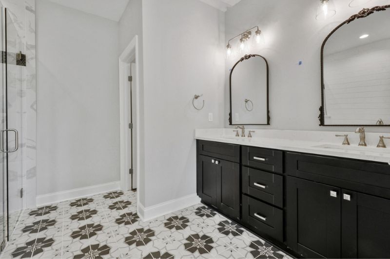 Bathroom with black vanity, white countertop, patterned floor tile, arched mirrors, and glass shower.