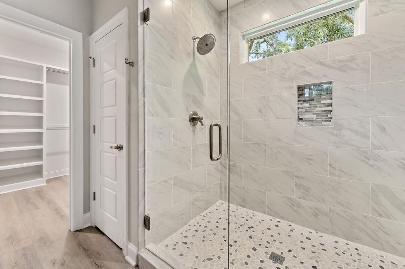 Bathroom with a glass shower, marble-like tile, and a walk-in closet with shelves.