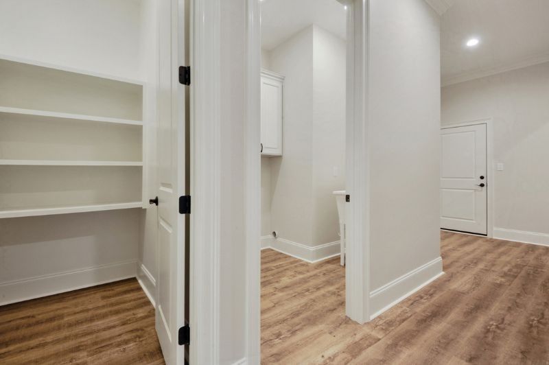 A bright, empty hallway with hardwood floors and doorways leading to storage and laundry.
