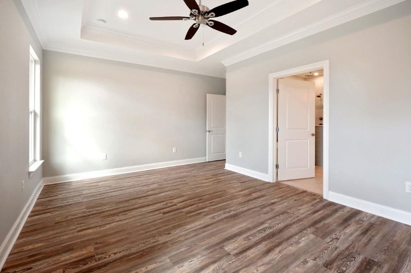 Empty bedroom with light gray walls, wood floor, white trim, and ceiling fan.