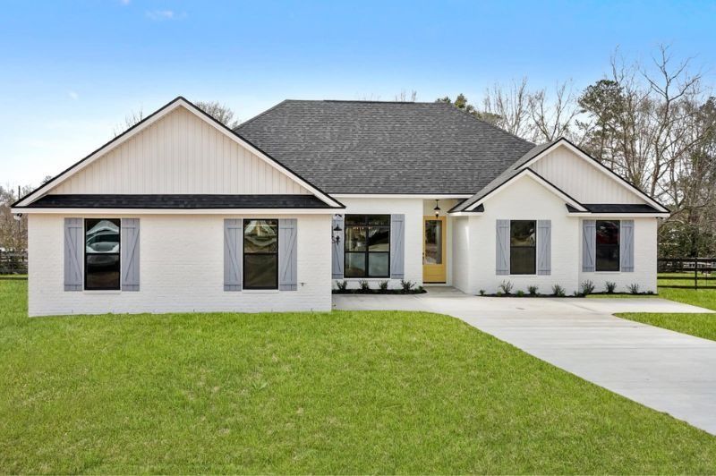 White house with black roof and gray shutters, on green lawn with clear sky.