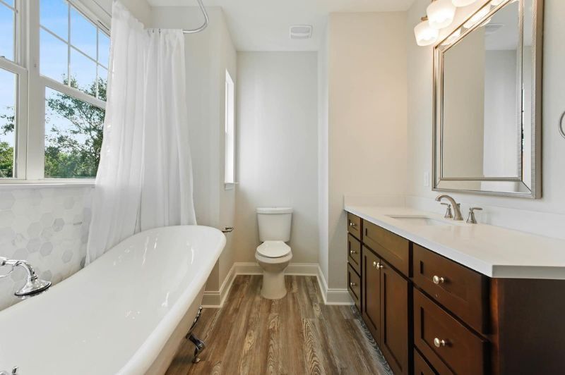 Bathroom with white tub, wood vanity, and large window.