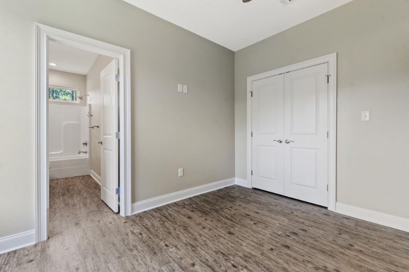 Empty room with gray walls, white trim, wood-look flooring, and two white doors, one to a bathroom.