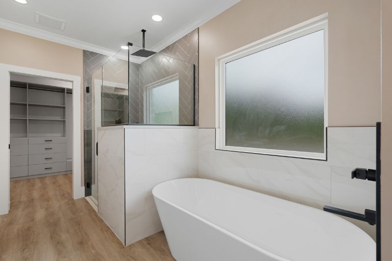 Modern bathroom with white soaking tub, glass shower, and walk-in closet.