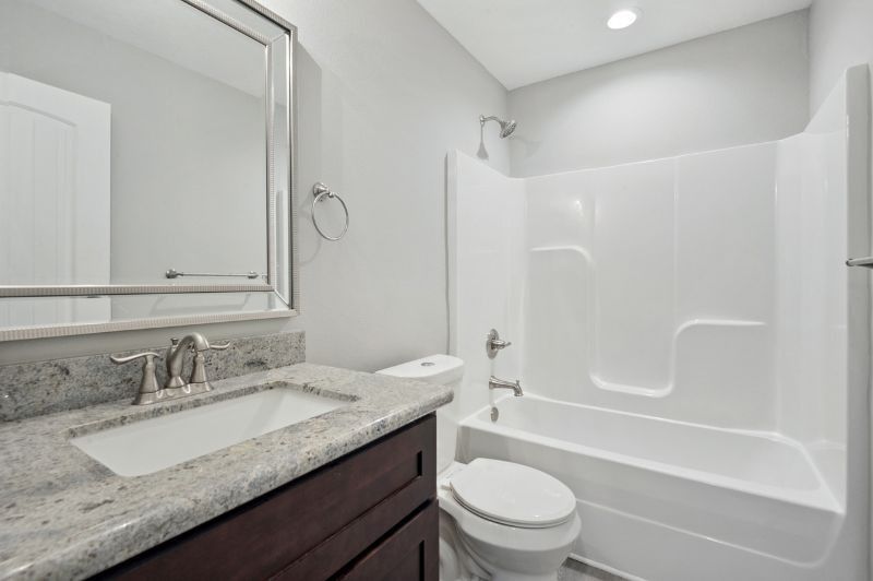 Bathroom with white tub and toilet, granite countertop, dark wood vanity, and silver fixtures.