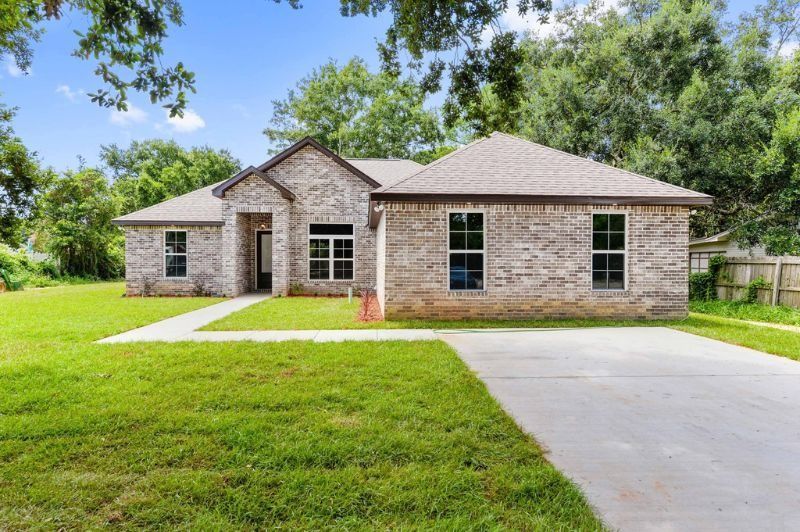 Single-story brick home with gray roof and driveway, set in a grassy yard.