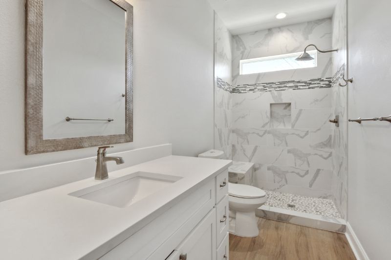 White bathroom with a sink, toilet, and shower. Light wood-look floor, marble-look shower wall, and a rectangular mirror.