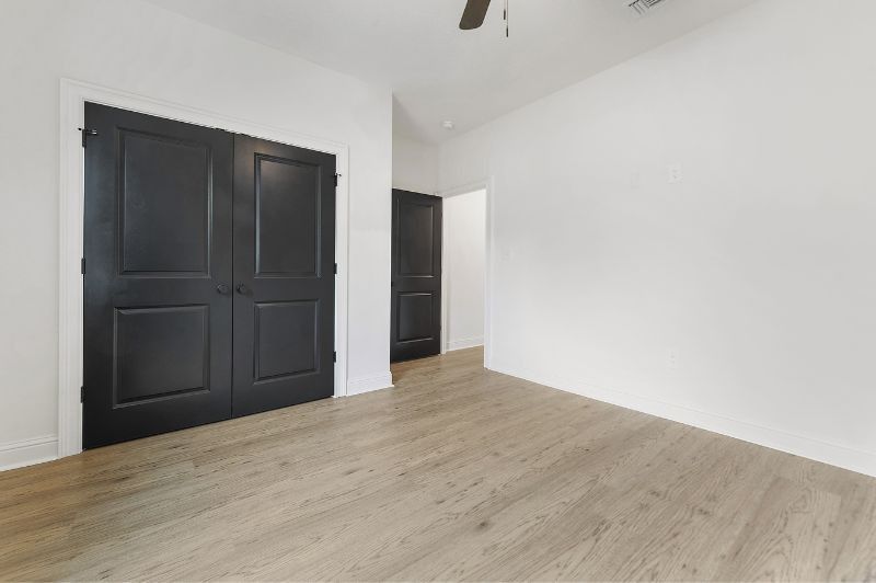 Empty room with black doors and light wood floor, white walls.