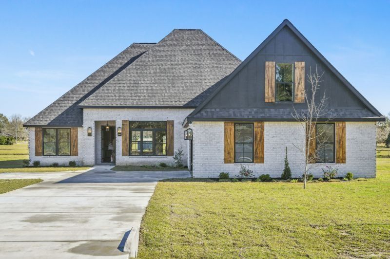 White brick house with gray roof and black gable, wood shutters on a sunny day.