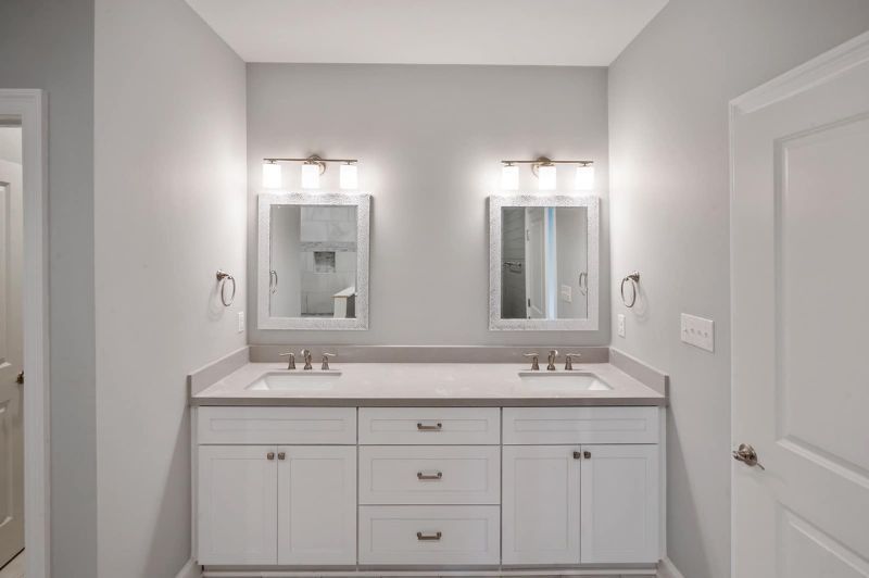 Bathroom with dual sinks, white cabinetry, gray countertop, mirrors, and lighting fixtures.