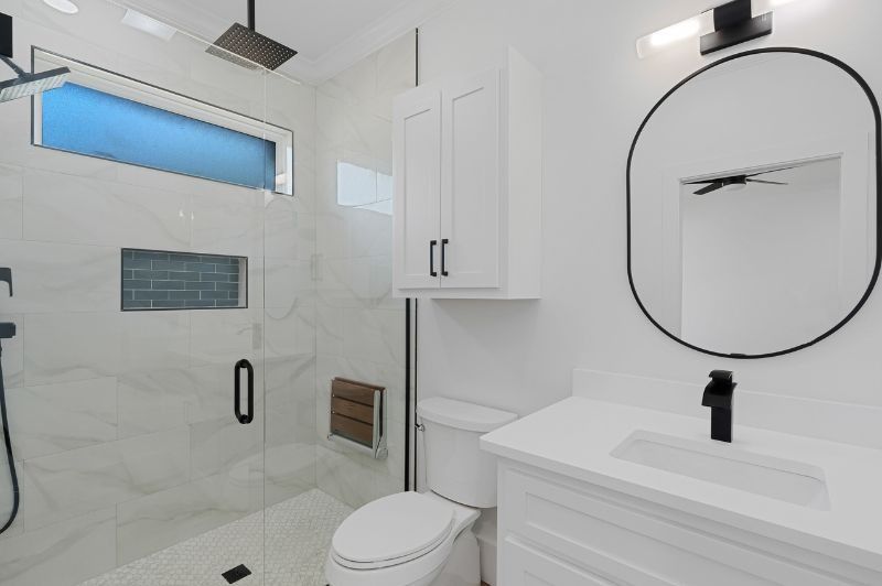 Modern white bathroom with shower, toilet, and vanity; black fixtures and accents.