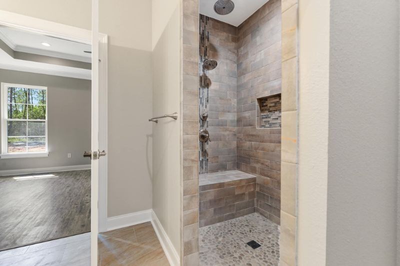 Bathroom with tiled shower, shower bench, and doorway to bedroom.