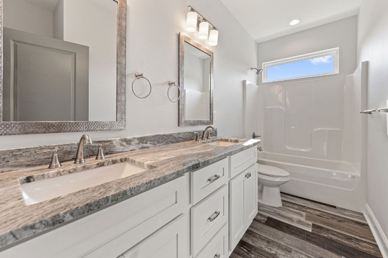 Modern bathroom with double vanity, large mirrors, and white tub and toilet.