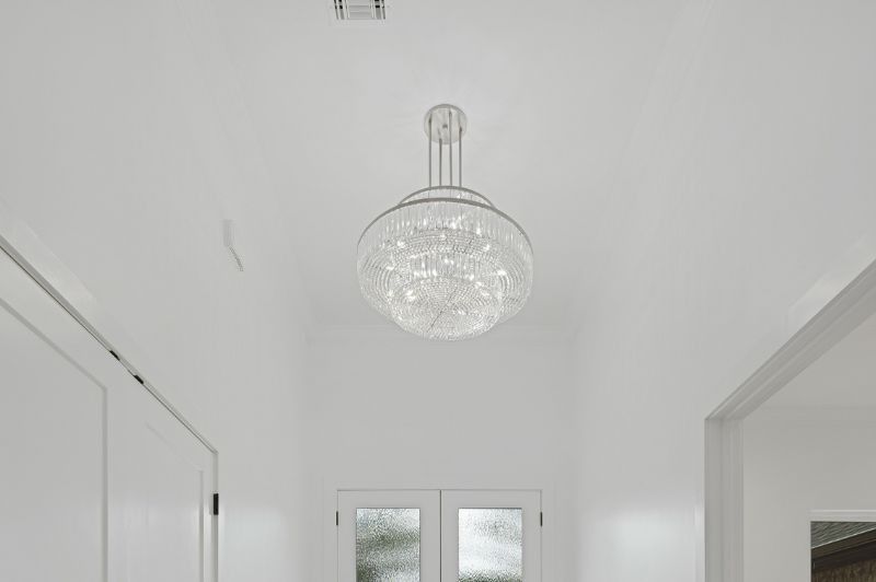 Bright white hallway with a large crystal chandelier centered on the ceiling.