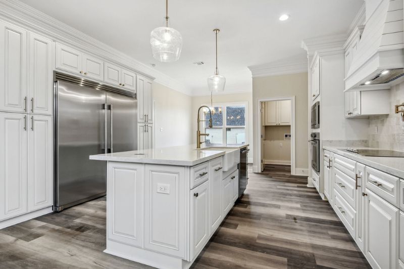 White kitchen with stainless steel refrigerator, island, and wood-look flooring.