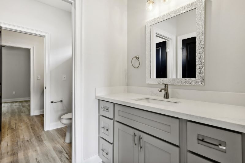 Bathroom with gray vanity, white countertop, framed mirror, and a door leading to a hallway with a toilet.