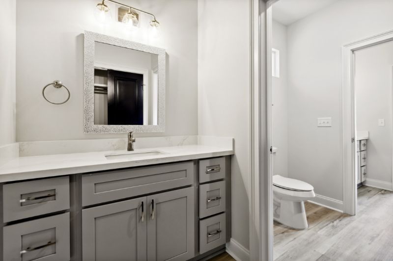 Bathroom with gray vanity, white countertop, mirror, and open door to a toilet.