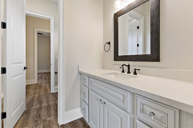 Bathroom with white vanity, black fixtures, dark-framed mirror, and dark wood-look flooring.