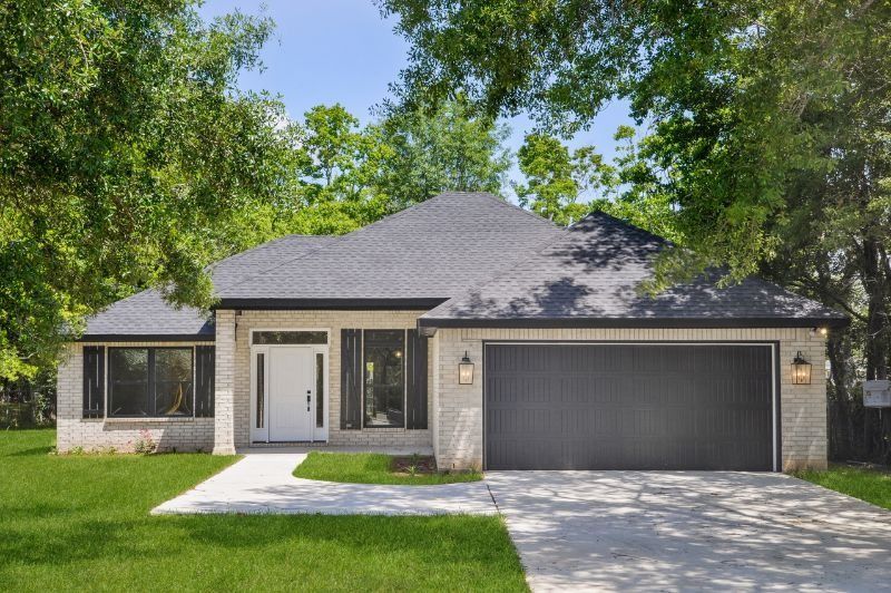 Ranch-style house with grey brick exterior, black roof, and a two-car garage; surrounded by trees and grass.