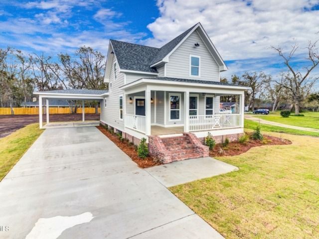 Light gray two-story house with a porch and carport, set on a green lawn under a blue sky.
