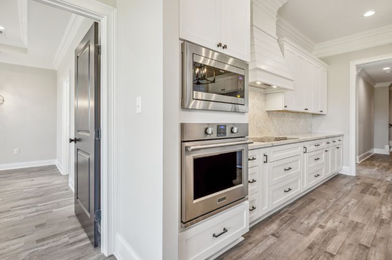 White kitchen with built-in oven and microwave; dark door on the left and hardwood floors.