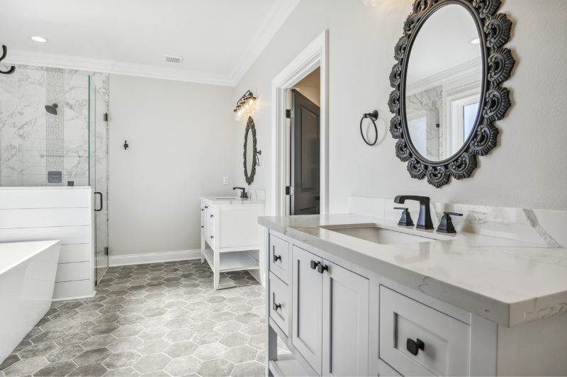 Bathroom with white vanities, ornate black-framed mirrors, and gray hexagon floor tiles.
