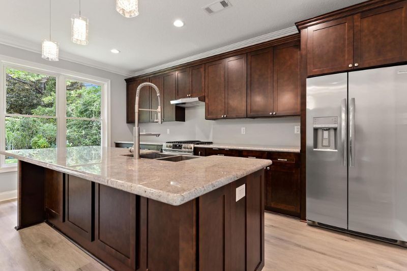 Modern kitchen with dark wood cabinets, granite countertops, and stainless steel refrigerator and appliances.